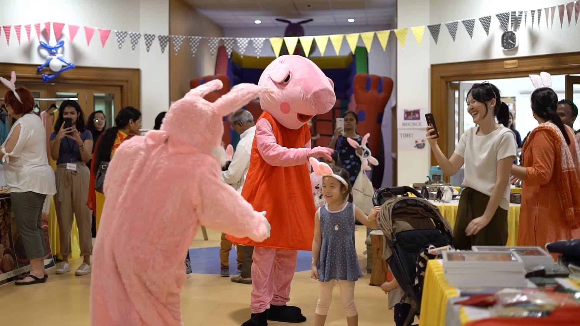 Teachers, parents and children with the cartoon characters Peppa pig and Rabbit in a carnival at IVS.