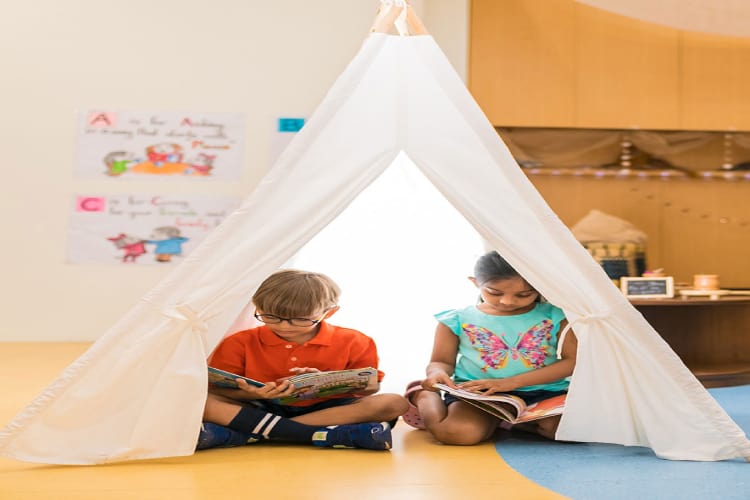 A small boy and a girl reading inside a tipi reading corner in the classroom.